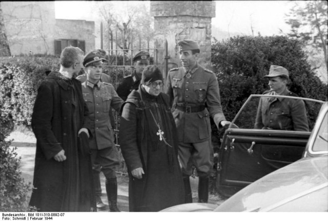 An Italian priest is helped into a car during the evacuation of the Abbey. On the right with his hand on the car door is General Fridolin von Senger und Etterlin with a Ritterkreuz.