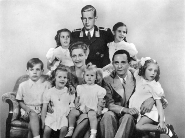 Goebbels Family portrait: in the center are Magda Goebbels and Joseph Goebbels, with their six children. Behind is Harald Quandt in the uniform of a Flight Sergeant of the Air Force. By Bundesarchiv – CC BY-SA 3.0 de