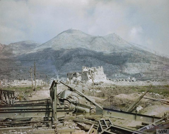 The_ruins_of_Cassino,_May_1944-_a_wrecked_Sherman_tank_and_Bailey_bridge_in_the_foreground,_with_Monastery_Ridge_and_Castle_Hill_in_the_background._TR1799