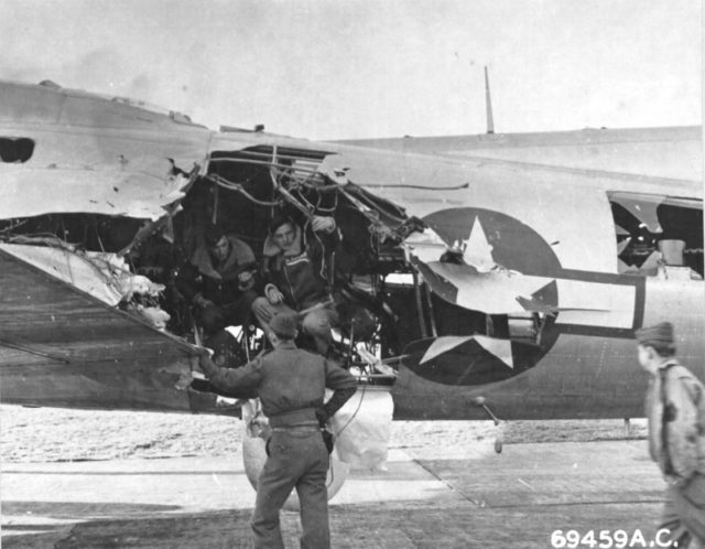 Crews examine flak damage to B-17G Fortress at RAF Bassingbourn, Cambridgeshire, England, UK. Damage sustained on mission to Munich, Germany, Jul 6 1944. Note "Mickey" pathfinder radar dome in place of ball turret (United States National Archives).