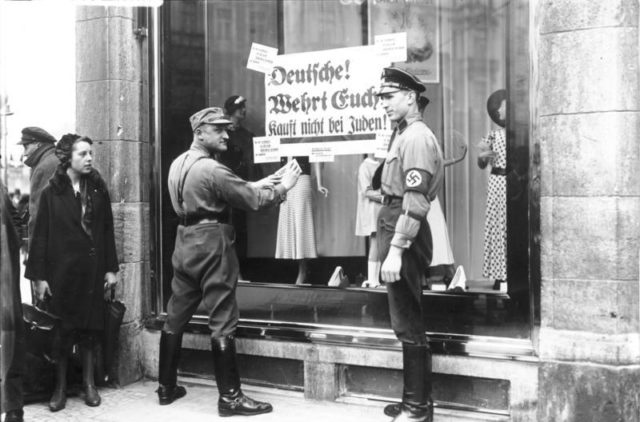 SA paramilitaries outside a Berlin store posting signs with: "Deutsche! Wehrt Euch! Kauft nicht bei Juden!" ("Germans! Defend yourselves! Do not buy from Jews!"). Photo Credit.
