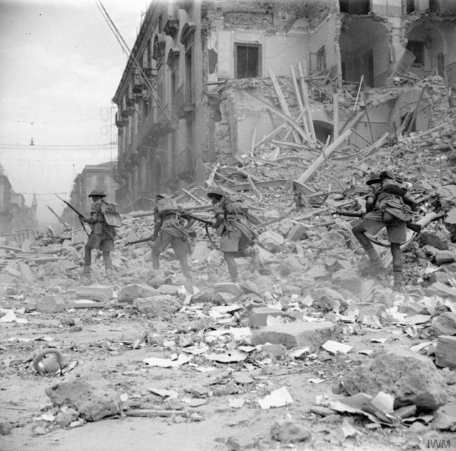 Infantry scramble over rubble in a devastated street in Catania, 5 August 1943. © IWM (NA 5335)