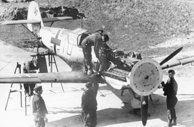 The synchronization gear of a Messerschmitt Bf 109E is adjusted (January 1941). A wooden disk attached to the propeller is used to indicate where each round passes through the propeller arc. Photo Credit.