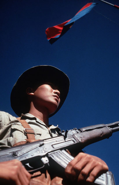 Viet Cong soldier stands beneath a Viet Cong flag carrying his AK-47 rifle. He was participating in the exchange of POWs by the Four Power Joint Military Commission.