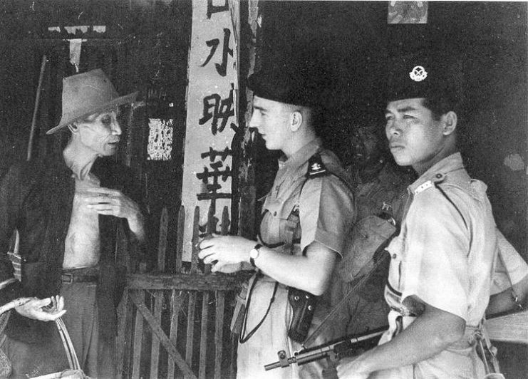 Police officers question a civilian during the Malayan Emergency.