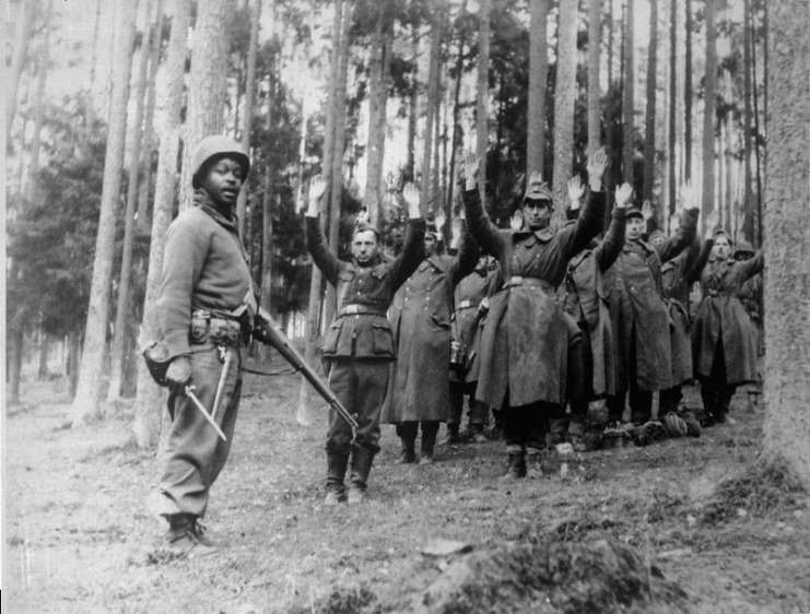This soldier of the 12th Armored Division is standing guard over a group of German prisoners in April 1945.
