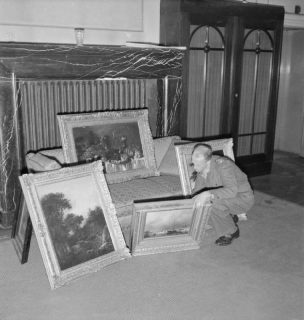 Captain H. H. Davies of Birkenhead, checks a collection of paintings found in the house of a member of the SS in Hanover who had looted them from Holland. Captain Davies was in charge of the Property Control Department of the Military Government, his job being to take over Nazi controlled buildings and property, including looted works of art. The latter were held for safe keeping until returned in due course to their rightful owners.