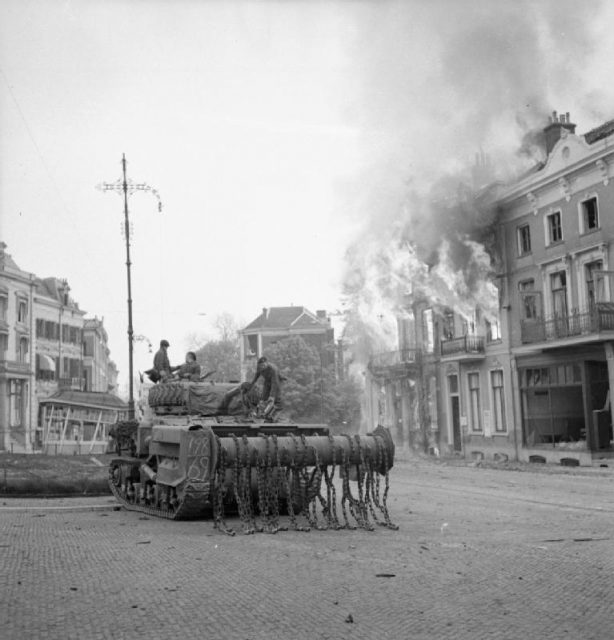 A Sherman Crab flail tank in front of burning buildings in Arnhem, 14 April 1945.