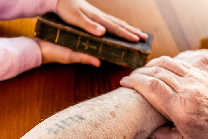 Close Up Hands Of Great Grandmother With Auschwitz Concentration Camp Number Showing Old Holy Bible