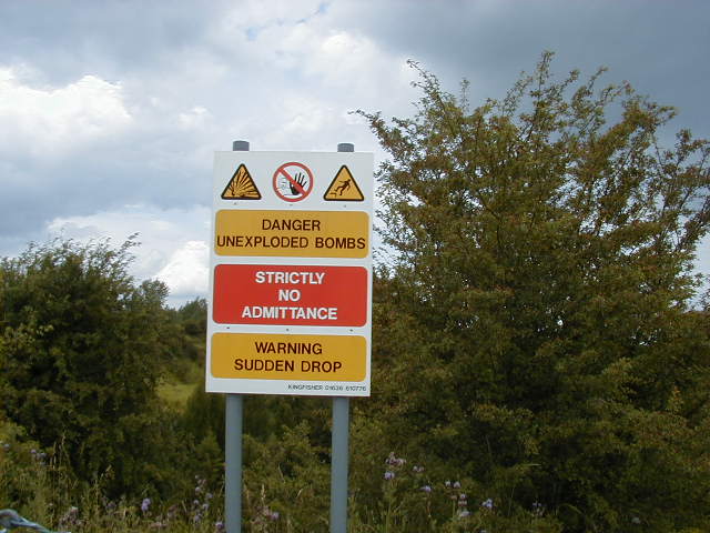Sign warning of unexploded munitions and hazard posed by the crater Photo by Trevman99 CC BY 2.5