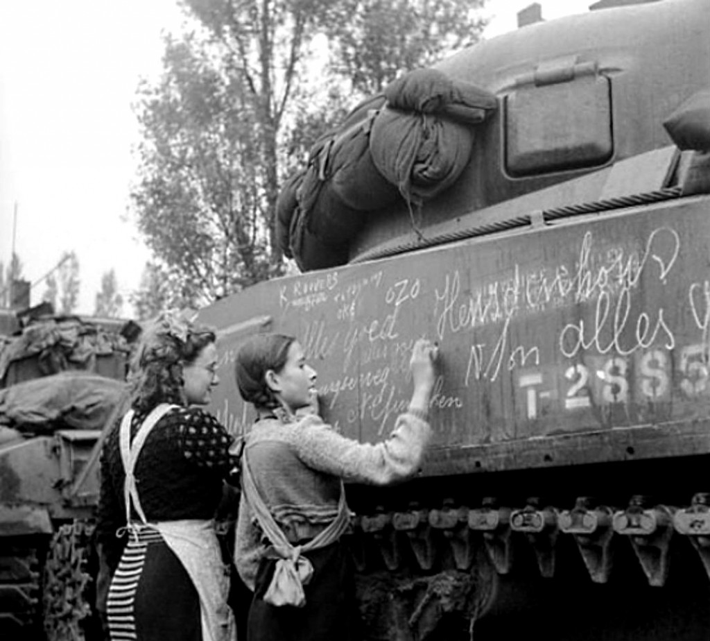 wo Dutch girls use chalk to write slogans and messages for friends and relatives in other towns on a tank after the liberation of Breda by the Allied Polish 1st Armoured Division. Many civilians in occupied countries would write messages on the tanks of their liberators, knowing that these tanks would soon move on to the next town, hoping their friends or relatives would see the messages. On the tank you can see names, addresses and “Alles goed” (“All is good” in Dutch). Breda, North Brabant, the Netherlands. November 1944.