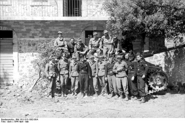 German and Italian troops pose in front of a Sturmgeschütz (tank) in the not yet destroyed town of Cassino.