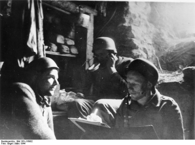 The German caption states: "a German paratrooper has made his hole into a living-bunker.  It's cramped but warm and cosy. A far better location than being outside on the streets".