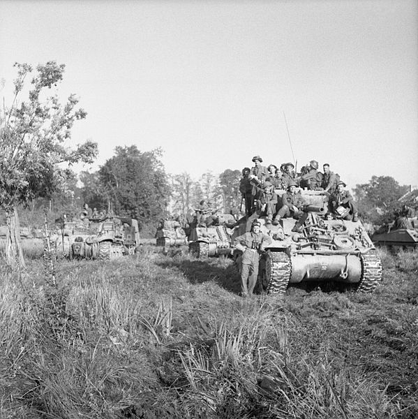 Sherman_tanks_carrying_infantry_wait_to_advance_at_the_start_of_Operation_'Goodwood',_Normandy,_18_July_1944._B7511