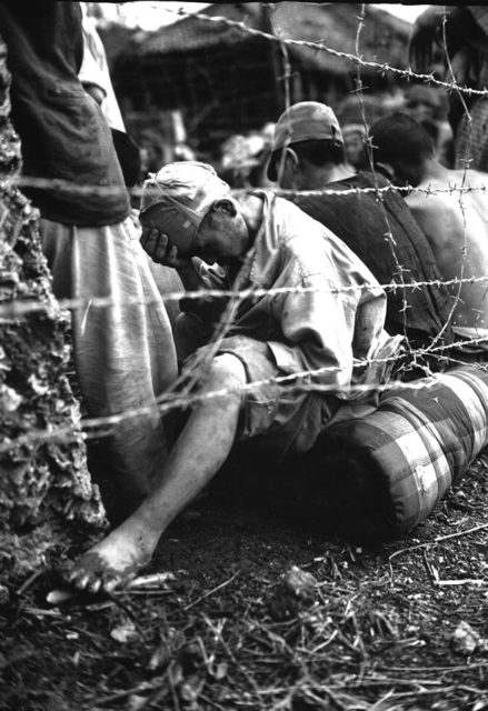 A Japanese prisoner of war sits behind barbed wire after he and 306 others were captured within the last 24 hours of the battle by 6th Marine Division.