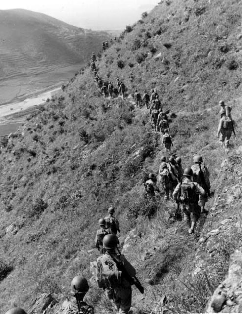 U.S. Marines move out over rugged mountain terrain while closing with hostile North Korean forces.
