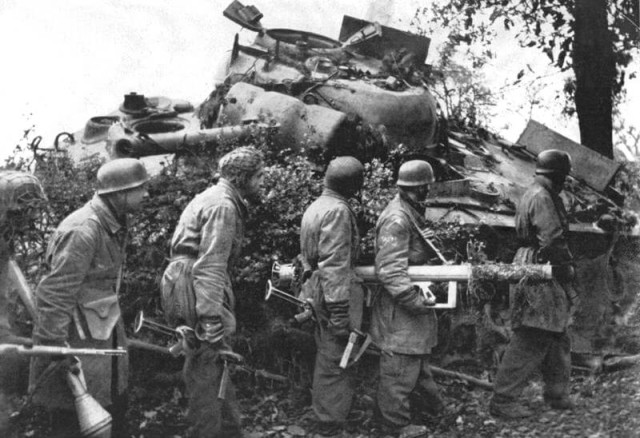 Heavily armed Fallschirmjager alongside a knocked-out Sherman. Note men with tank-killing Panzerschreck and Panzerfaust weapons (Image).