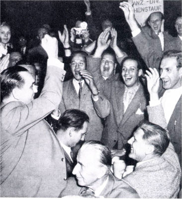 Jubilant crowd at a HIAG convention. Kurt Meyer standing with his fist in the air, while Paul Hausser looks on.