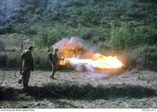 3rd Battalion, The Royal Australian Regiment (3RAR), pioneers using a flamethrower to clear undergrowth from the perimeter wire in the area known as The Horseshoe. Note the fire extinguisher and fire-proof blanket carried by the soldier at left. (Donor B. Betts) [© AWM (P02222.017)/ CC-BY-SA 3.0]