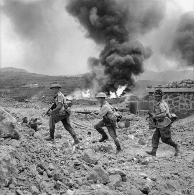 Men of 1st Battalion, The Duke of Wellington's Regiment, advance past a burning fuel store on Pantelleria. Left to right: Lance Sergeant A Haywood, Private C Norman and Private H Maw. [© IWM (NA 3668)]
