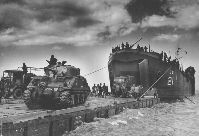  The U.S. Coast Guard manned USS LST-21 unloads British Army tanks and trucks onto a "Rhino" barge during the early hours of the invasion on Gold Beach [1], 6 June 1944. Note the nickname "Virgin" on the "Sherman" tank at left.