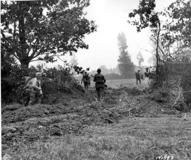 GI's move forward through breach in hedgerow made by bulldozer. 9th div. France. 25/07/44. By Unknown American soldier - Archives de la Mache, Saint Lo, Public Domain, https://commons.wikimedia.org/w/index.php?curid=20193988