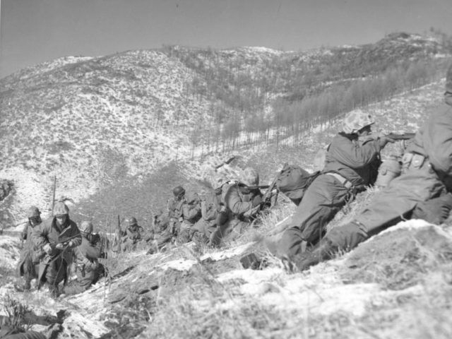 Marines under the cover of a large boulder engaging the Chinese during the Korean War