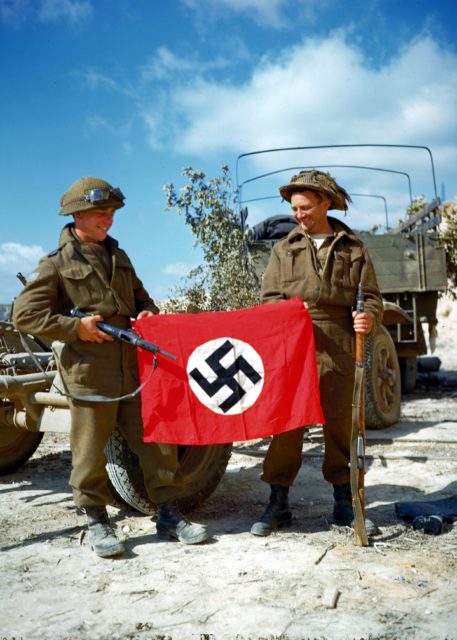 Canadian troops posing with a captured German flag, 10 August 1944; note Sten gun and Lee-Enfield rifle (Public Domain)