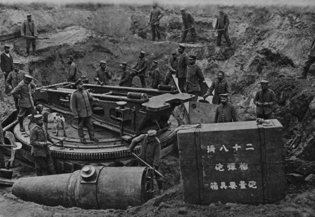 German soldiers excavating a Japanese 28 cm. siege howitzer near Grodno; a munitions or spare parts crate sitting to the side.