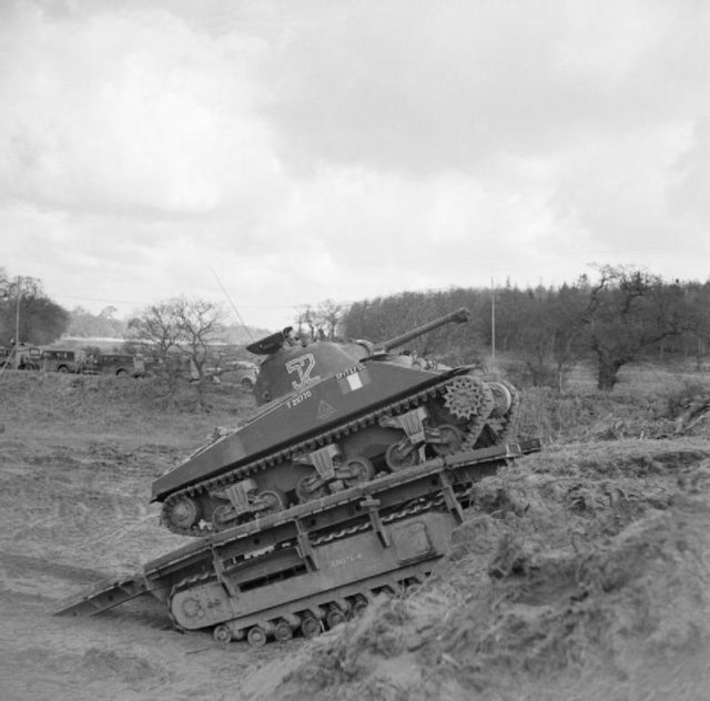 A Sherman tank uses a Churchill Ark to climb an escarpment during a training exercise. Photo Credit.