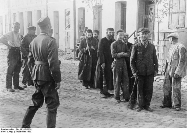Polish Jews are lined up by German soldiers to do forced labor, September 1939. Bundesarchiv – CC BY-SA 3.0 de