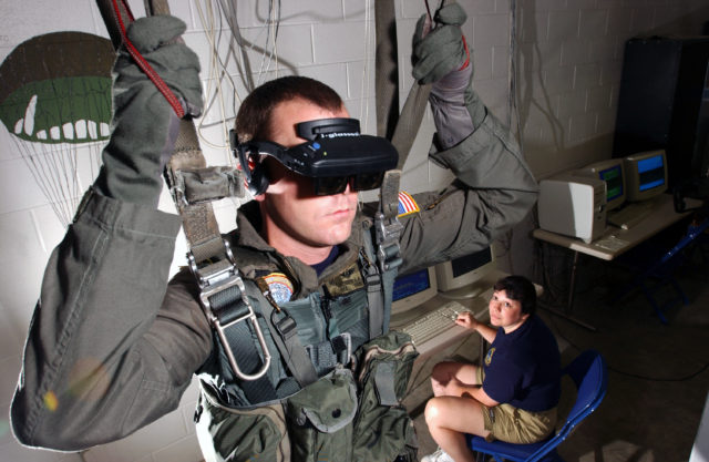 021115-N-5862D-001 Aboard Naval Air Station (NAS) Pensacola (Nov. 15, 2002) -- Hospital Corpsman 2nd Class Tim Sudduth, from Vashowish, Wash., demonstrates the Virtual Reality (VR) parachute trainer, while Aviation Survival Equipmentman 1st Class, Jackie Hilles, from Ekland, Penn., controls the program from a computer console. Students wear the VR glasses while suspended in a parachute harness, and then learn to control their movements through a series of computer-simulated scenarios. The computer receives signals from the student as they pull on the risers that control the parachute. The VR trainer also teaches aircrew personnel how to handle a parachute in different weather conditions and during possible equipment malfunctions. Navy and Marine Corps aviators receive state of the art training at the Naval Survival Training Institute. U.S. Navy photo by Chief PhotographerÕs Mate Chris Desmond. (RELEASED)