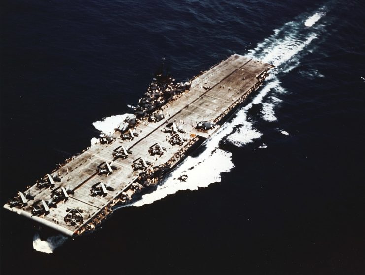 The U.S. Navy aircraft carrier USS Yorktown (CV-10) underway, circa in mid-1943, possibly during her shakedown cruise in the late spring. Planes on deck include Grumman F6F-3 Hellcat fighters and Curtiss SB2C-1 Helldiver dive bombers. Note this carrier’s unique longitudinal black flight deck stripe and the absence of any hull numbers on the flight deck.