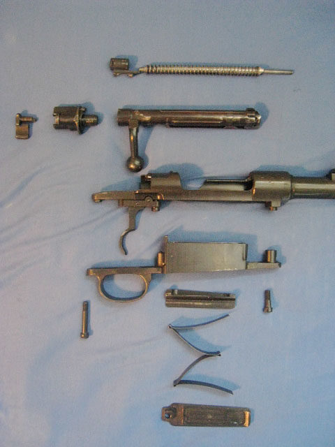 Partially disassembled Mauser Karbiner 98k action, with a receiver in the middle, magazine well and magazine assembly below and disassembled bolt on top. Photo: Mauseraction, CC BY-SA 3.0.