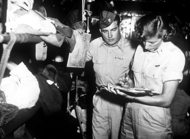 Medical: Evacuation. Combat Cargo, Japan. Flight nurse, 1st Lt Victoria Malokas, Cleveland, OH, checks a patient’s progress chart in flight. Pilots like Maj George E. Cichy, San Pedro, CA, a U.S. Air Force C-54 aircraft commander, often briefs interested patients on the aircraft’s position, altitude, and other information.U.S. Air Force photo