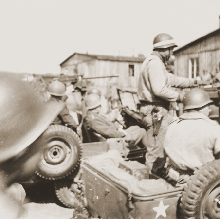 General George S. Patton (seated in the middle jeep) arrives  at the newly liberated Ohrdruf concentration camp in the company of a large group of American troops;
