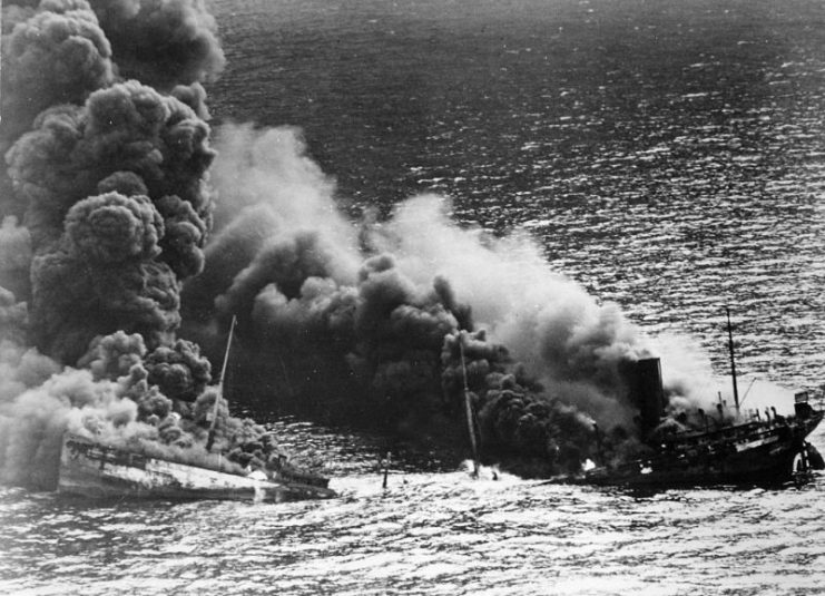 Allied tanker torpedoed in Atlantic Ocean by German submarine. Ship crumbling amidship under heat of fire, settles toward bottom of ocean, 1942.