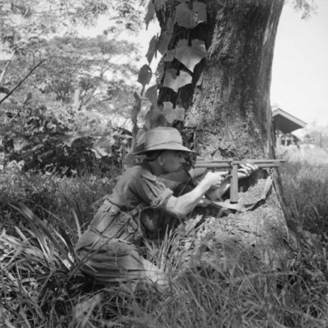 A squad leader of the Royal Scots Fusiliers provides covering fire with his M1 Thompson submachine gun in the village of Namma, Burma, in October 1944.