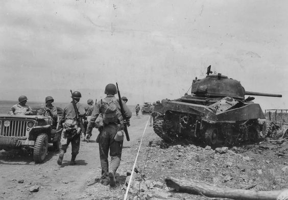 GIs walk past a knocked out M4 Sherman at the Anzio Front