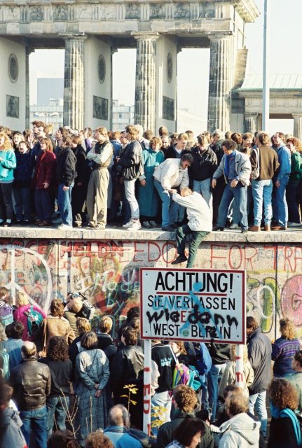 People atop the Berlin Wall near the Brandenburg Gate on 9 November 1989. Photo: Sue Ream – CC BY 3.0