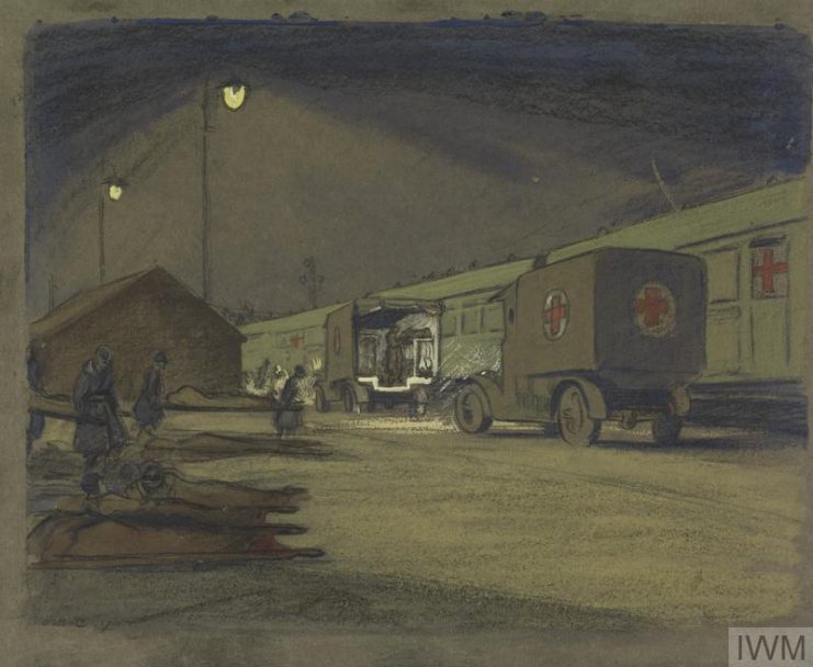 Two motor ambulances have pulled up alongside a stationary ambulance train, with casualties being unloaded. IWM