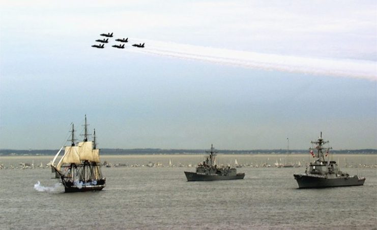 USS Constitution fires her guns in salute while underway in Massachusetts Bay, escorted by the frigate USS Halyburton (FFG-40) (center) and the destroyer USS Ramage (DDG-61) (right), as the United States Navy’s “Blue Angels” pass overhead. Commissioned on 21 October 1797, Constitution set sail unassisted for the first time in 116 years.