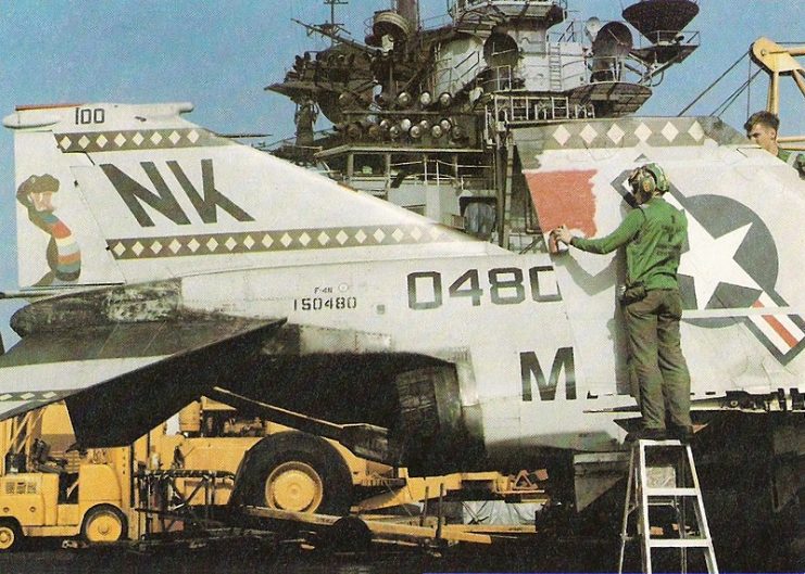 A U.S. Marine Corps McDonnell F-4N Phantom II aircraft (BuNo 150480) of Marine fighter-attack squadron VMFA-323 Death Rattlers on the aircraft carrier USS Coral Sea (CV-43) in April 1980. Sailors are applying black-red-black identification stripes for the (later aborted) attempt to rescue U.S. hostages from Iran, code named “Operation Eagle Claw” (or “Evening Light”).