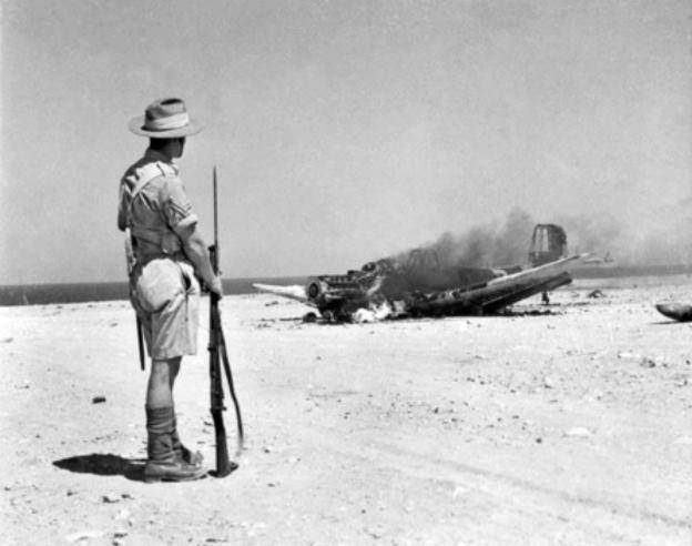 Australian soldier observing the burning wreck of Ju 87B Stuka dive bomber, near Tobruk, Libya, 1941.