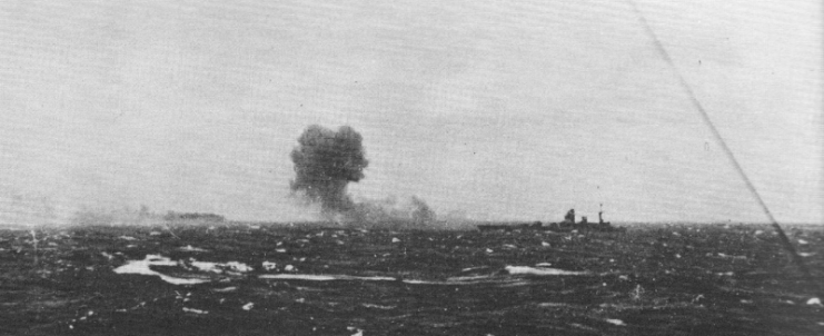 Rodney firing on Bismarck, which can be seen burning in the distance