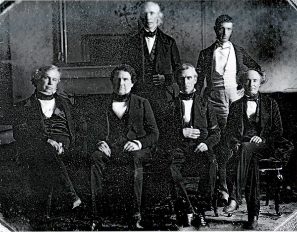 Polk and his cabinet in the White House dining room, 1846. Front row, left to right: John Y. Mason, William L. Marcy, James K. Polk, Robert J. Walker. Back row, left to right: Cave Johnson, George Bancroft. Secretary of State James Buchanan is absent. This was the first photograph taken in the White House, and the first of a presidential Cabinet.