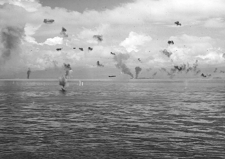 Japanese Navy Type 1 land attack planes (Mitsubishi G4M1 “Betty”) fly low through anti-aircraft gunfire during a torpedo attack on U.S. Navy ships maneuvering between Guadalcanal and Tulagi in the morning of 8 August 1942. The burning ship in the center distance is probably USS George F. Elliott (AP-13), which was hit by a crashing Japanese aircraft during this attack.