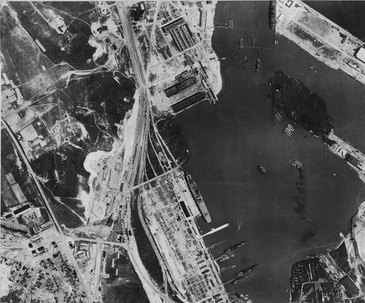 The German aircraft carrier Graf Zeppelin photographed on 6 February 1942 at Gotenhafen (today Gdynia, Poland) by a British Royal Air Force aircraft. A three-masted sailing ship, possibly one of the German Navy’s vessels (Horst Wessel (1936), Albert Leo Schlageter (1937), or Gorch Fock (1933)), appears at a nearby pier.