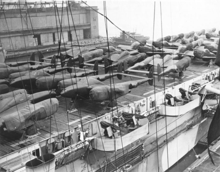 Cocooned Lockheed P-38 Lightnings and North American Aviation P-51 Mustangs line the decks of a U.S. Navy Escort “Jeep” Carrier (CVE) ready for shipment to Europe from New York.