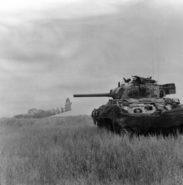 A Sherman DD amphibious tank of 13th/18th Royal Hussars in action against German troops using crashed Horsa gliders as cover near Ranville, Normandy, 10 June 1944.